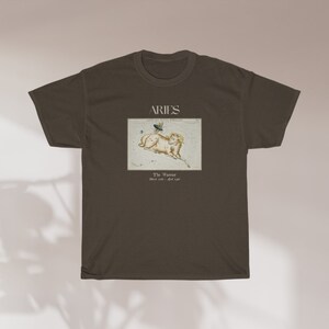 Pu&ograve; includere: Una maglietta marrone con un'illustrazione vintage della costellazione dell'Ariete. L'illustrazione &egrave; in una cornice bianca con il testo "Aries The Ram March 21 - April 19".