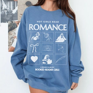 Puede incluir: Una sudadera azul con el texto "HOT GIRLS READ ROMANCE" y una cuadr&iacute;cula de nueve ilustraciones blancas, que incluyen un coraz&oacute;n, un lazo, un libro, una flecha, una pluma y una persona leyendo. El texto "A BOOK CLUB BY BOOKED READER GIRLS" est&aacute; impreso debajo de la cuadr&iacute;cula.