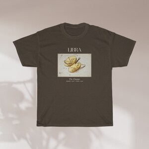 May include: A dark brown t-shirt featuring a Libra zodiac design. The graphic includes the word "LIBRA" above an illustration of the scales, with text below indicating the dates September 23 - October 22.