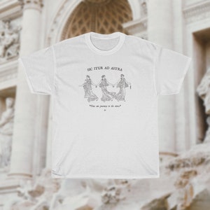 May include: White t-shirt with a black and white illustration of three women holding hands. The text "Sic Itur Ad Astra" is above the illustration and the text "This is our journey to the stars" is below the illustration.