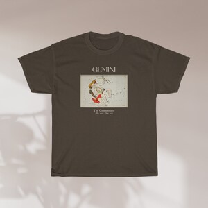 Pode incluir: Uma camiseta marrom escura com uma estampa gr&aacute;fica da constela&ccedil;&atilde;o de G&ecirc;meos. O texto "GEMINI" e "The Twins" est&aacute; impresso na camiseta.