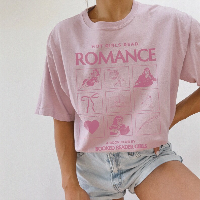 May include: A pink t-shirt with the text "HOT GIRLS READ ROMANCE" and a grid of illustrations. The text "A BOOK CLUB BY BOOKED READER GIRLS" is at the bottom of the shirt.