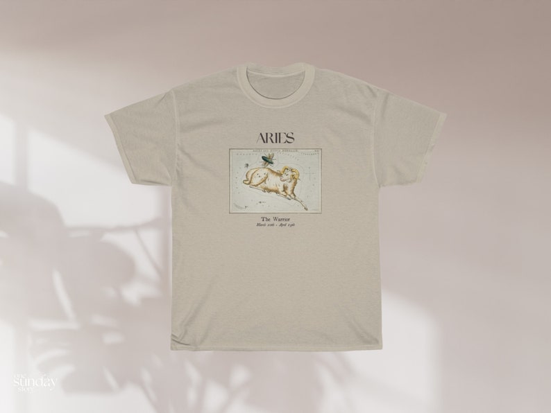 Pu&ograve; includere: Una t-shirt beige con una stampa grafica della costellazione dell'Ariete. La grafica include il testo "Aries" e "The Ram" con le date dal 21 marzo al 19 aprile.