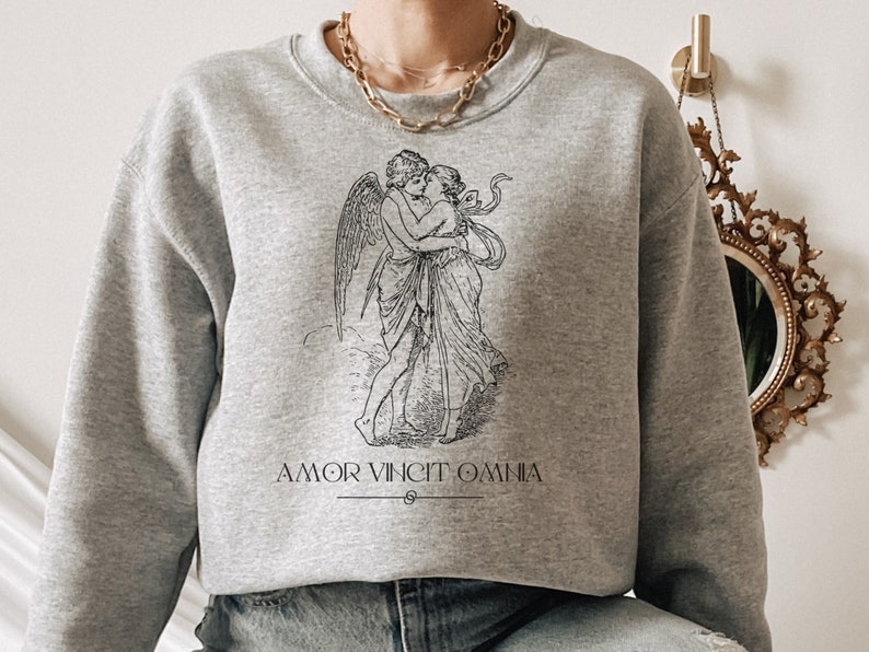 May include: A gray sweatshirt with a black and white illustration of a couple embracing. The text "AMOR VINCIT OMNIA" is printed below the illustration.