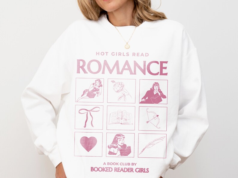 Puede incluir: Sudadera blanca con un gr&aacute;fico rosa que dice "Hot Girls Read Romance" y presenta una cuadr&iacute;cula de nueve im&aacute;genes que incluyen un coraz&oacute;n, un lazo, un libro, una flecha, una pluma y una mujer. El texto en la parte inferior dice "A Book Club by Booked Reader Girls."
