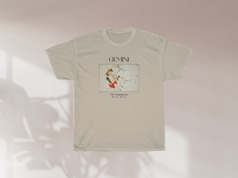 Pode incluir: Uma camiseta bege com uma estampa gr&aacute;fica da constela&ccedil;&atilde;o de G&ecirc;meos. O texto "GEMINI" e "The Communicators" est&aacute; impresso na camiseta.