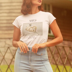 Pu&ograve; includere: Maglietta bianca con una grafica del segno zodiacale Ariete, un ariete con stelle, e il testo "Aries The Warrior March 21st - April 19th".