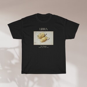 May include: Black t-shirt featuring the word "LIBRA" above a vintage-style illustration of the Libra zodiac symbol. The graphic includes the text "The Charmer" and the dates "September 23rd - October 22nd".