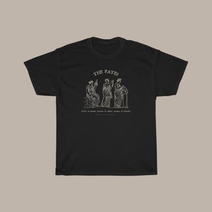 May include: Black t-shirt with a white graphic of three figures representing the Fates, with the text "THE FATES" above them. The text below the figures reads "Clotho the spinner, Lachesis the allotter, Atropos the inevitable."