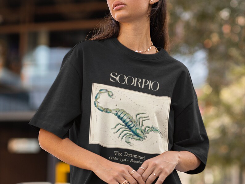 Op de afbeelding: Zwart T-shirt met een vintage illustratie van het sterrenbeeld Schorpioen en de tekst "Scorpio, The Determined, October 23rd - November 21st".