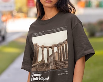 Könnte beinhalten: Ein braunes T-Shirt mit einem grafischen Druck einer antiken Ruine. Der Text auf dem Shirt lautet "Camp Half-Blood" und "Rules My D.D. & Chiron".