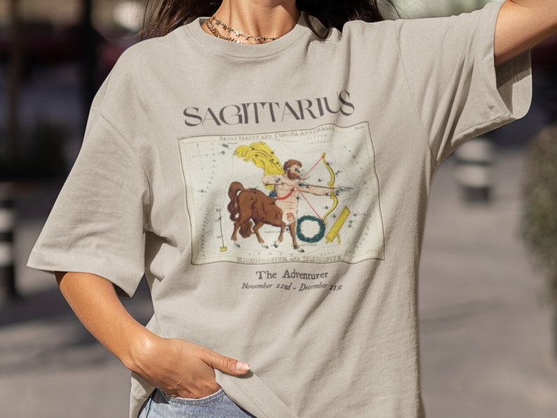 May include: A beige t-shirt with a vintage illustration of the Sagittarius constellation and the text "SAGITTARIUS The Adventurer November 22nd - December 21st".