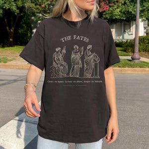 May include: Black t-shirt with a white graphic of three figures labeled "The Fates" and the text "Clotho the Spinner, Lachesis the Allotter, Atropos the Inevitable."