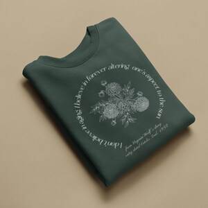 May include: A dark green sweatshirt with a white floral design and a quote from Virginia Woolf's diary, "I don't believe in aging I believe in forever altering one's aspect to the sun",  entry dated October 2nd, 1932.