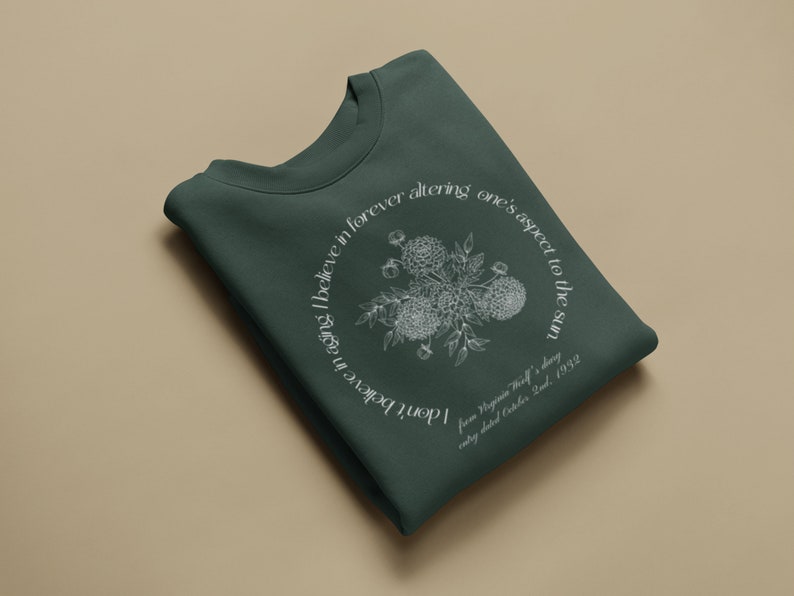 May include: A dark green sweatshirt with a white floral design and a quote from Virginia Woolf's diary, "I don't believe in aging I believe in forever altering one's aspect to the sun",  entry dated October 2nd, 1932.