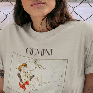 Pode incluir: Uma camiseta bege claro com uma ilustra&ccedil;&atilde;o vintage da constela&ccedil;&atilde;o de G&ecirc;meos e a palavra "GEMINI" impressa em preto.