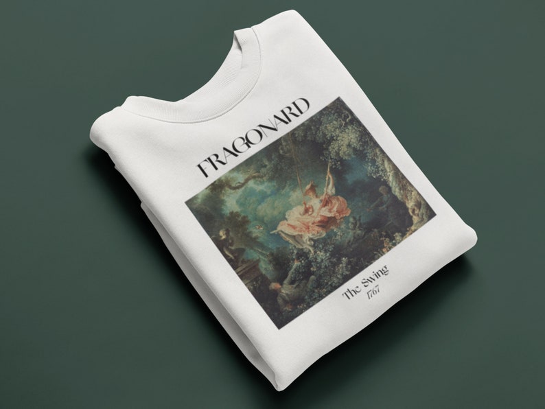 May include: White t-shirt with a print of a painting by Jean-Honor&eacute; Fragonard called "The Swing" from 1767. The painting depicts a woman on a swing in a garden setting.
