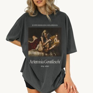 May include: A dark gray t-shirt with a painting of Judith Beheading Holofernes by Artemisia Gentileschi (1614-1652).