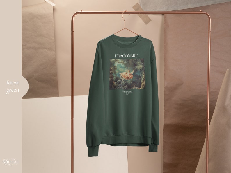 May include: Forest green sweatshirt with a painting of a woman in a boat on the front. The painting is titled "The Swing" by Fragonard.