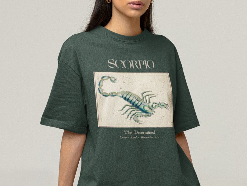 Op de afbeelding: Een donkergroen t-shirt met een vintage illustratie van een schorpioen en de tekst "SCORPIO The Determined October 23rd - November 21st"