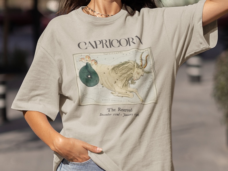 May include: A beige t-shirt with a vintage illustration of the Capricorn constellation and the text "Capricorn The Reserved December 22nd - January 19th".
