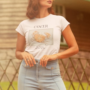 May include: White t-shirt with a graphic of a crab and the text "Cancer The Nurturer You feel it, you lead."