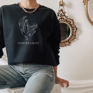 May include: Black sweatshirt with a white graphic of a woman with wings and the text "VENI VIDI AMA VI".
