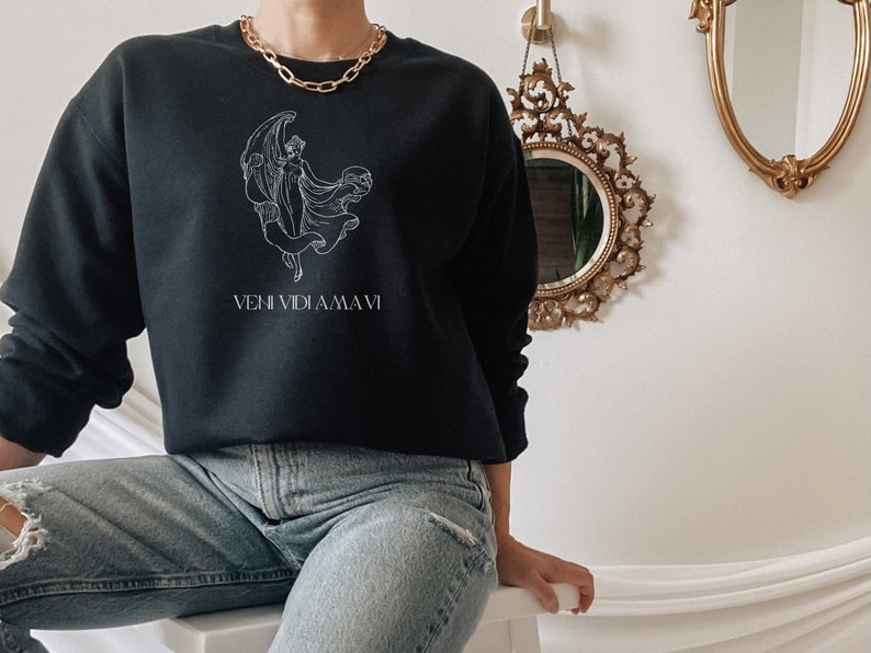May include: Black sweatshirt with a white graphic of a woman with wings and the text "VENI VIDI AMA VI".