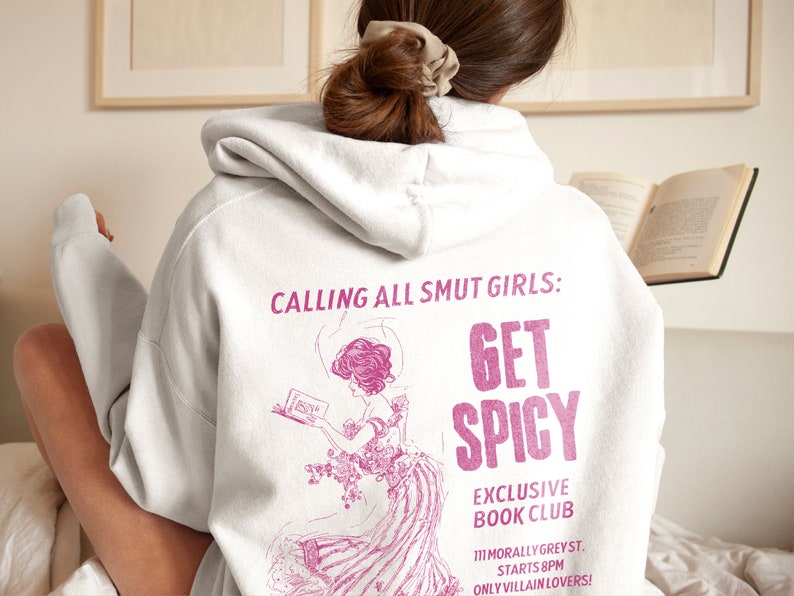 May include: A white hoodie with a pink graphic print that says "Calling all smut girls: Get Spicy" and "Exclusive Book Club" with a pink illustration of a woman reading a book. The text also says "111 Morally Greyst. Starts 8PM Only Villain Lovers!"