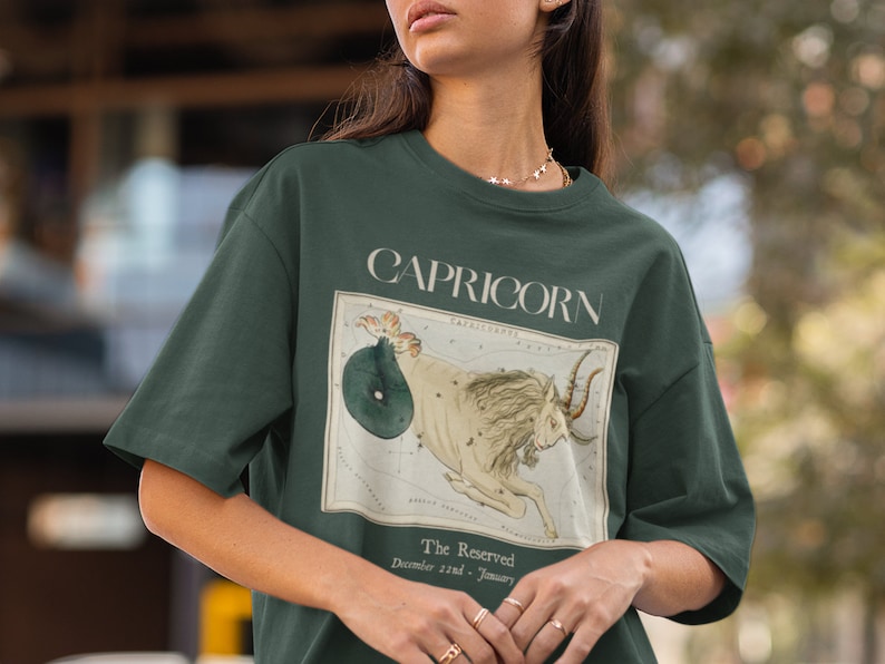 May include: A dark green t-shirt with a vintage illustration of the Capricorn zodiac sign. The illustration is surrounded by a white border and includes the text "Capricorn" and "The Reserved, December 21st - January 19th".