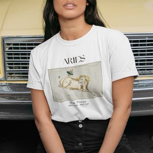 Pu&ograve; includere: Maglietta bianca con un'illustrazione vintage della costellazione dell'Ariete e il testo "ARIES The Warrior March 21st - April 19th".