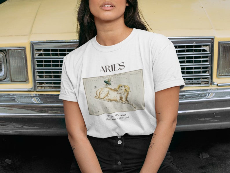 Pu&ograve; includere: Maglietta bianca con un'illustrazione vintage della costellazione dell'Ariete e il testo "ARIES The Warrior March 21st - April 19th".