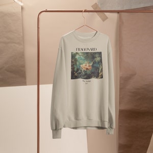 May include: A beige sweatshirt with a print of a painting by Fragonard, "The Swing", on the front. The text "FRAGONARD" and "The Swing 1767" is printed below the image.