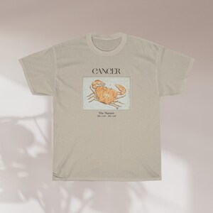 May include: A beige t-shirt with a graphic of a crab and the text "Cancer The Narcissist June 21st - July 22nd".