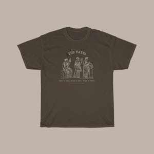 May include: A brown t-shirt with a white graphic of three figures labeled "The Fates". The text below the figures reads "Clotho the spinner, Lachesis the allotter, Atropos the inevitable".