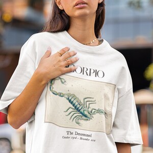 Op de afbeelding: Wit T-shirt met een grafische print van een schorpioen en de tekst "Scorpio, The Determined, October 23rd - November 21st".