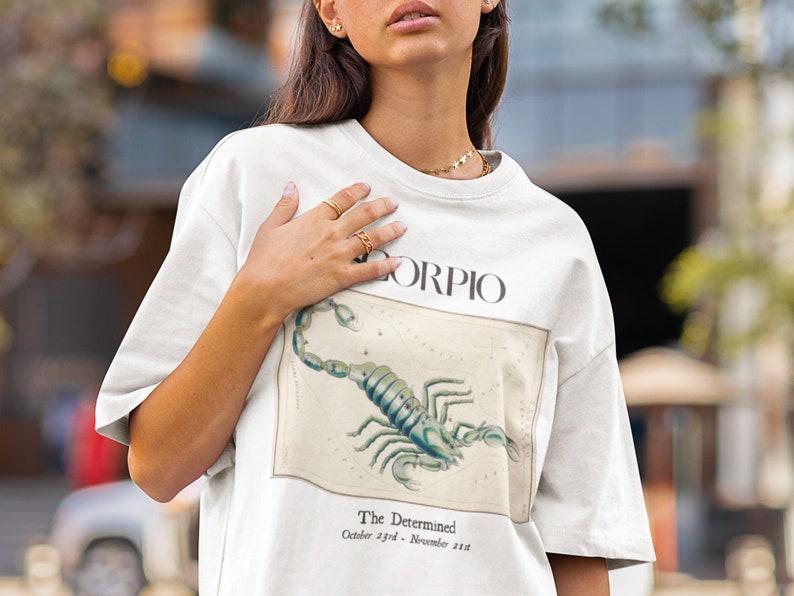 Op de afbeelding: Wit T-shirt met een grafische print van een schorpioen en de tekst "Scorpio, The Determined, October 23rd - November 21st".
