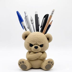 May include: A tan-colored desk organizer shaped like an angry bear with its arms crossed. The bear's head holds pens and pencils, including a blue pen, silver pens, a black pen, a pencil, and a black pencil. The bear has a stern expression.