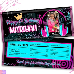May include: A pink and blue chocolate bar wrapper with a black background. The wrapper features a cartoon image of a girl wearing headphones and a crown. The text "Happy 6th Birthday MARIYAH" is printed on the wrapper. The back of the wrapper has a nutrition facts label with a fun, colorful design.