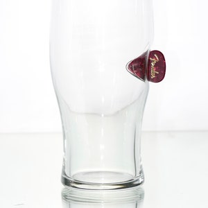 May include: A clear glass pint glass with a red Fender guitar pick attached to the side.