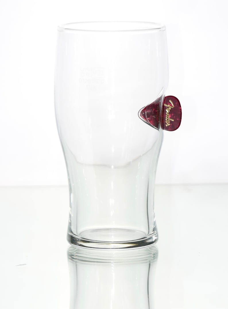 May include: A clear glass pint glass with a red Fender guitar pick attached to the side.