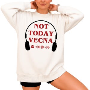 May include: A cream-coloured sweatshirt featuring the red text "NOT TODAY VECNA" within a black headphone outline. A Spotify logo and soundwave graphic are below. The sweatshirt is a casual, long-sleeved garment.