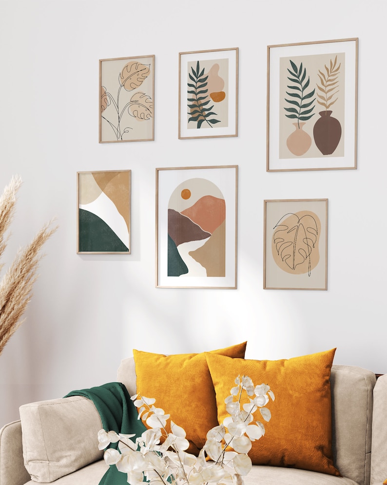 May include: A gallery wall with six framed prints featuring abstract line drawings of plants and landscapes in shades of brown, green, and orange. The prints are arranged in a symmetrical pattern on a white wall.
