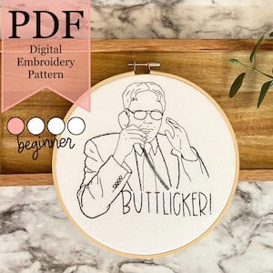 May include: A black and white embroidery pattern of a man on the phone with the text "BUTTLICKER!" on a white background. The pattern is in a hoop and is labeled as a beginner embroidery pattern.