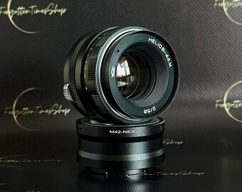 May include: A black camera lens with the text "HELIOS-44M 2/58" printed on the side. The lens is attached to a black adapter with the text "M42-NEX" printed on it.