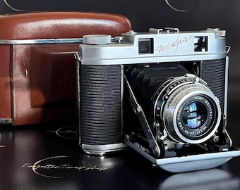 May include: A silver and black vintage camera with a leather case. The camera has a lens with the text "Helios-44-2 58mm 1:2" and "USSR" printed on it. The camera also has the text "Москва" printed on the top.