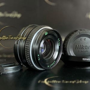 May include: A black Nikon F mount lens with a 52mm filter thread. The lens is a manual focus lens and has a silver ring around the barrel. The lens is in good condition and has a few scratches on the barrel.