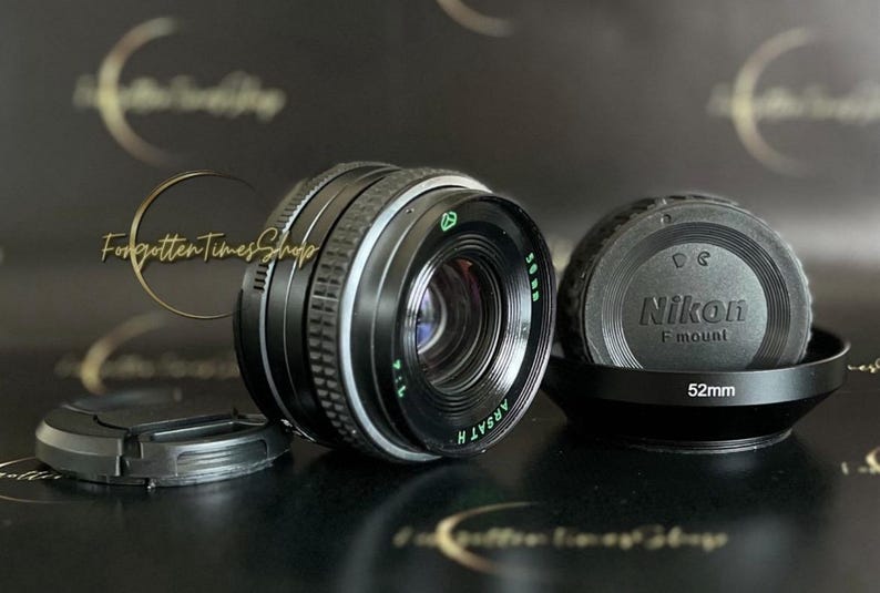 May include: A black Nikon F mount lens with a 52mm filter thread. The lens is a manual focus lens and has a silver ring around the barrel. The lens is in good condition and has a few scratches on the barrel.
