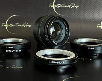 May include: A black camera lens with a silver ring and the text "JUPITER-8 2/50" printed on it. Three black camera lens adapters are also pictured, labeled "L39-NEX", "L39-FX", and "L39-M4/3".
