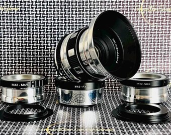 May include: A collection of camera lens adapters and a lens. The lens is black with silver accents and the text "HELIOS-44M-4". The adapters are silver and black, with text indicating their compatibility, including "M42-FX" and "M42-NEX".
